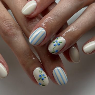 Short oval cream nails with blue vertical stripes and tiny blue floral accents