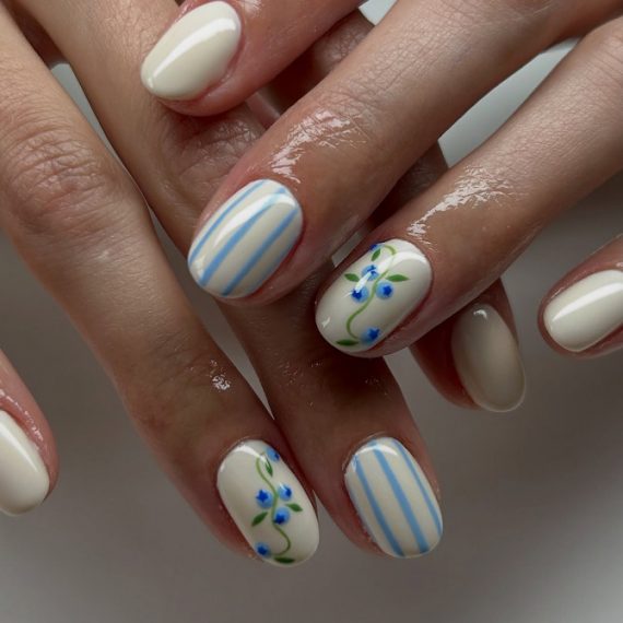 Short oval cream nails with blue vertical stripes and tiny blue floral accents