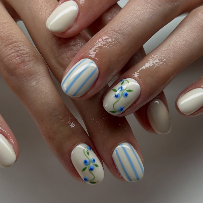 Short oval cream nails with blue vertical stripes and tiny blue floral accents