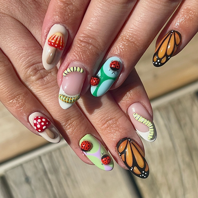 Almond-shaped nails with butterfly wings, ladybug charms, red mushrooms, and forest-inspired insect nail art