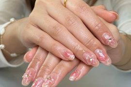 Oval nails with pink marble swirls, 3D petal accents, and silver gem embellishments