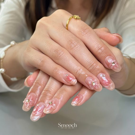 Oval nails with pink marble swirls, 3D petal accents, and silver gem embellishments