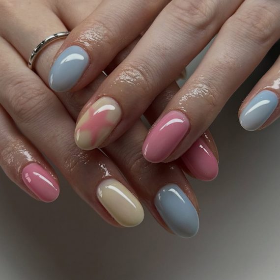 Glossy oval nails in pastel pink, blue, and yellow with one watercolor-blend accent nail