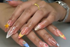 Long almond nails with nude base, 3D flowers, dotted tips, ocean waves, and pearl embellishments