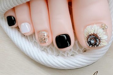 Bold pedicure with alternating black, white, and gold glitter nails, finished with a 3D sunflower nail art on the big toe.