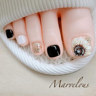 Bold pedicure with alternating black, white, and gold glitter nails, finished with a 3D sunflower nail art on the big toe.