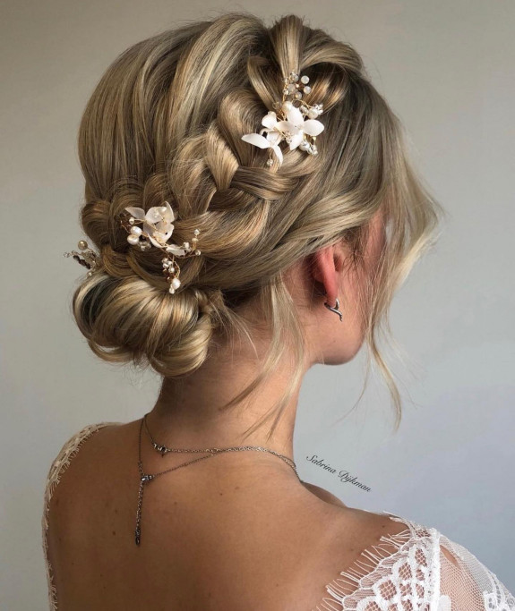 Braided bridal bun with blonde strands and white floral hairpins.