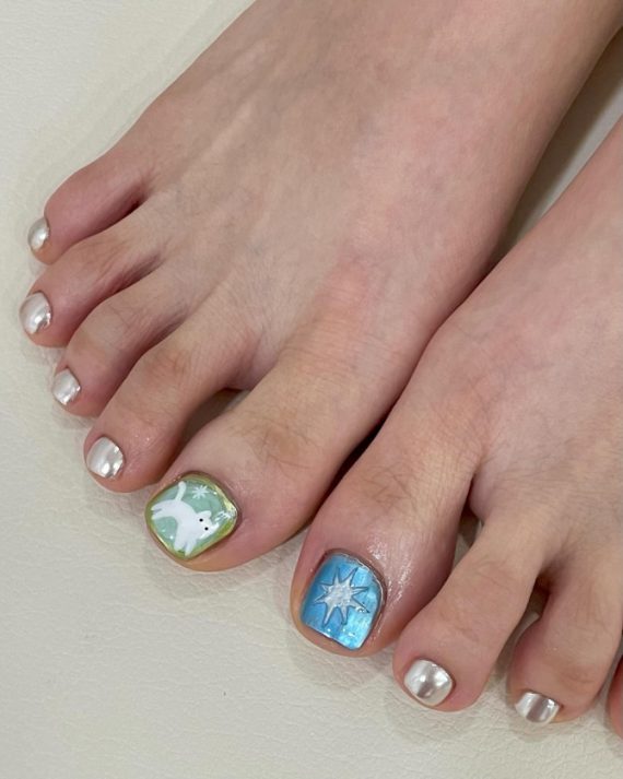 Toe nails with metallic silver polish and big toes featuring white dove on green and star art on blue background