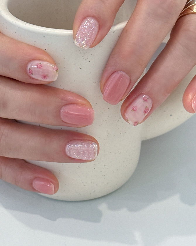 Short nude nails with cherry blossom floral decals, pink glitter accent, and soft natural finish.