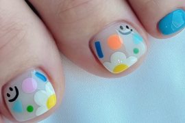 Toe nails with translucent base featuring smiley faces, colorful abstract shapes, and daisy flowers for a cheerful design