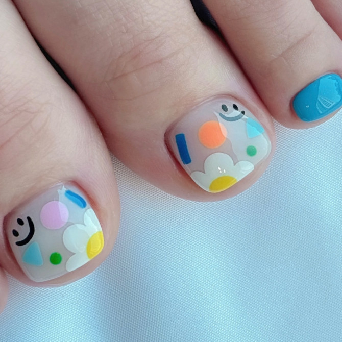 Toe nails with translucent base featuring smiley faces, colorful abstract shapes, and daisy flowers for a cheerful design