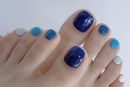 Toe nails painted in ombre shades from white and baby blue to navy, forming a fresh and summery gradient pedicure.