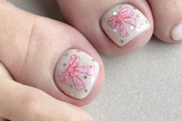 White toenails featuring pink ribbon bow art with glitter dots, designed for a soft and feminine spring look