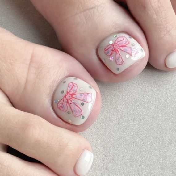 White toenails featuring pink ribbon bow art with glitter dots, designed for a soft and feminine spring look