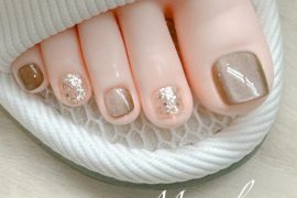 Elegant brown and gold glitter pedicure with shimmer polish on big toes and accent nails in soft neutral tones.