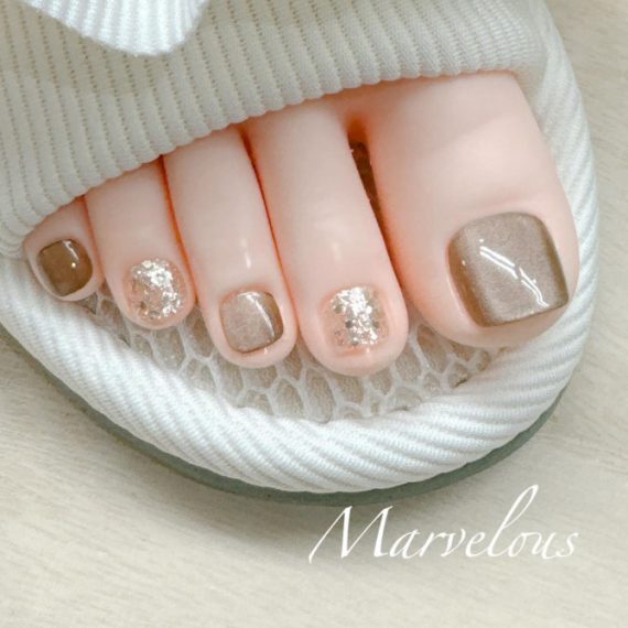 Elegant brown and gold glitter pedicure with shimmer polish on big toes and accent nails in soft neutral tones.