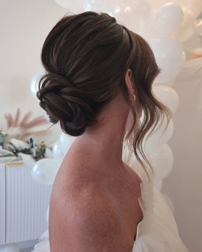 Dark bridal bun with soft tendrils, styled in a smooth twist.