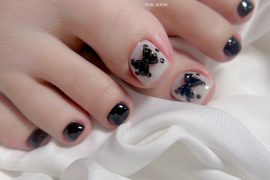 Toe nails with glossy black polish and nude base featuring 3D black bows and square nail shape
