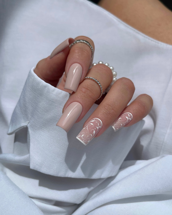Long nude coffin nails with glossy finish and intricate white scroll art on ring fingers, bridal-inspired.
