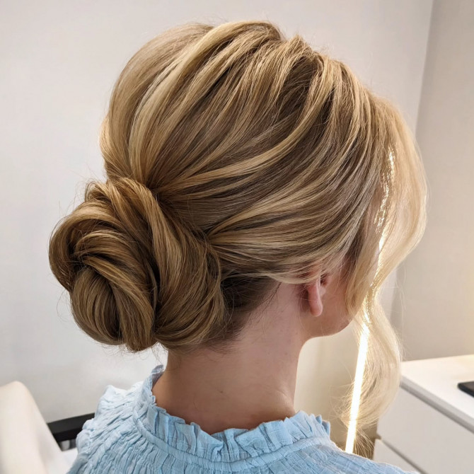 Classic low bridal bun with golden blonde strands and soft wave. Elegant bridal hairstyle with crown braid and floral bun.