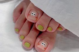 Toe nails with glossy olive green polish and hand-drawn cartoon face with wide eyes and blush on big toes