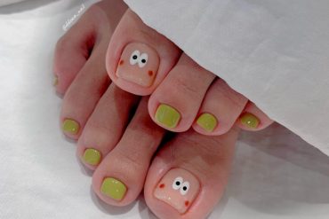 Toe nails with glossy olive green polish and hand-drawn cartoon face with wide eyes and blush on big toes