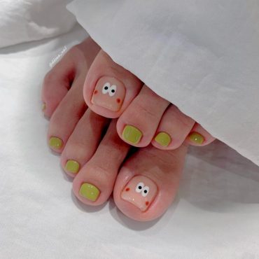 Toe nails with glossy olive green polish and hand-drawn cartoon face with wide eyes and blush on big toes