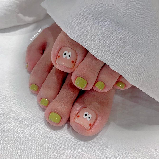 Toe nails with glossy olive green polish and hand-drawn cartoon face with wide eyes and blush on big toes