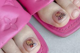 Toe nails with glittery pink polish featuring Hello Kitty beach-themed character art on big toes