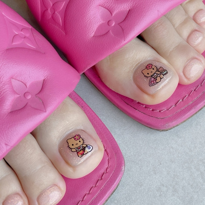 Toe nails with glittery pink polish featuring Hello Kitty beach-themed character art on big toes