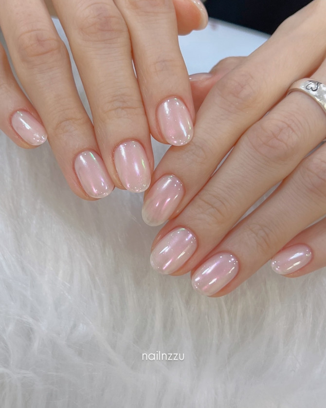 Short almond nails with a translucent pink nude shimmer on fair hands, minimal and glowing finish.