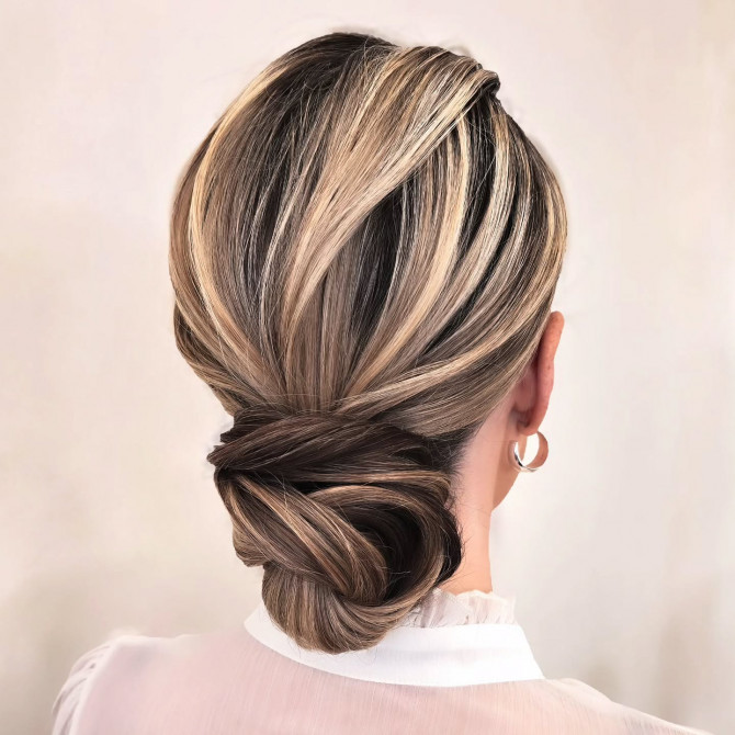 Elegant low twisted bridal updo with blonde and ash brown highlights.