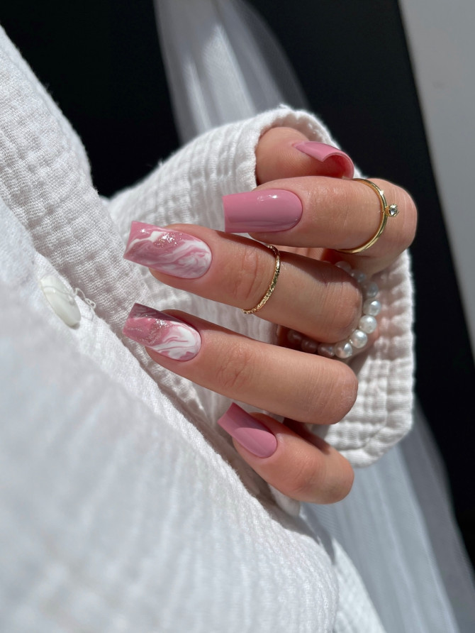 Long square-shaped nails in soft mauve with white marble accent art, worn with pearl and gold rings.