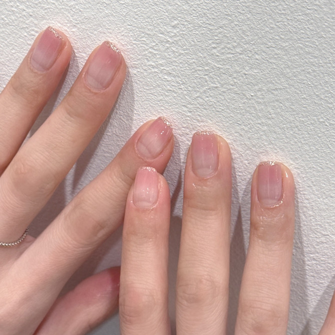 Short natural nails with sheer pink base and thin gold glitter tips on fair skin.
