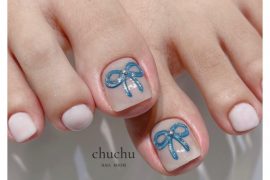 Nude toe nails with square shape featuring blue glitter bow accents on big toes