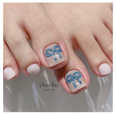 Nude toe nails with square shape featuring blue glitter bow accents on big toes