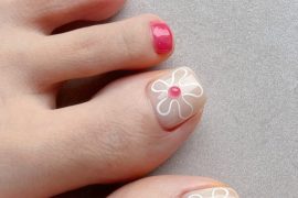 Toenails painted nude and hot pink with big toes featuring outlined white flowers and pink dot centers for a summer-ready pedicure.
