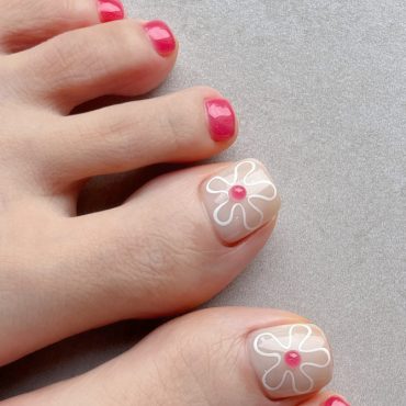 Toenails painted nude and hot pink with big toes featuring outlined white flowers and pink dot centers for a summer-ready pedicure.