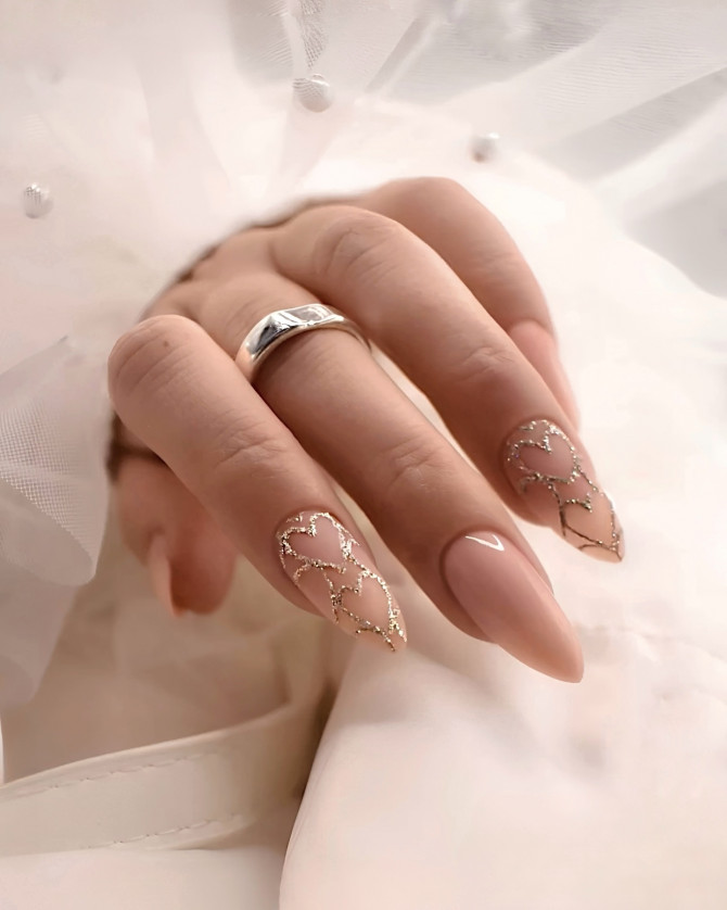 Nude almond bridal nails with gold glitter heart outlines on sheer base—elegant and romantic for modern wedding looks. 