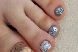 Toe nails with mixed blue shimmer textures, mosaic tiles, silver glitter, and a teddy bear design on a nude marble base