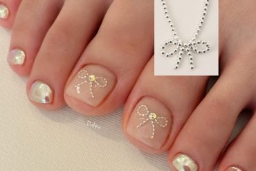 Pearl white toenails with shimmering crystal bow accents on the big toes, perfect for summer elegance