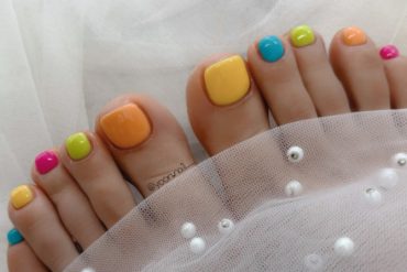 Colorful rainbow pedicure with glossy neon polish on each toe in candy-like tones