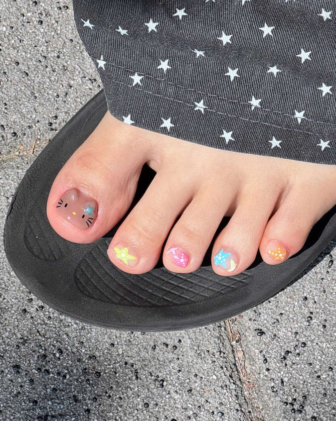 Cute rainbow-themed toe nails with a brown cat face and pastel star designs on each toe.