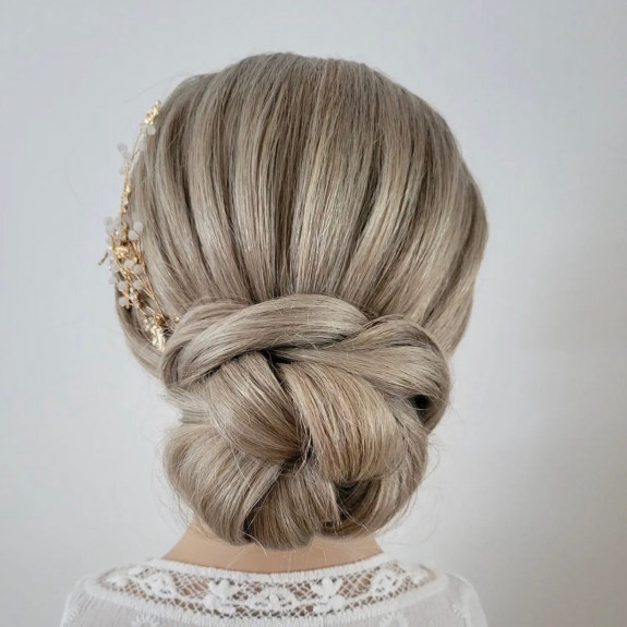 Platinum blonde bridal bun with braided twist and gold floral hairpin.