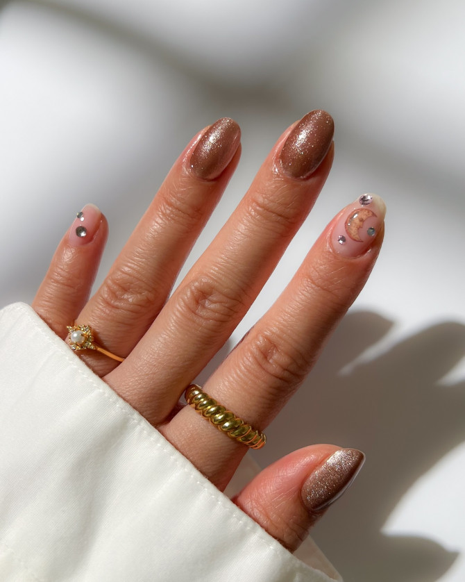 Mocha almond nails with shimmer finish and a moon-and-crystal celestial accent on a nude base