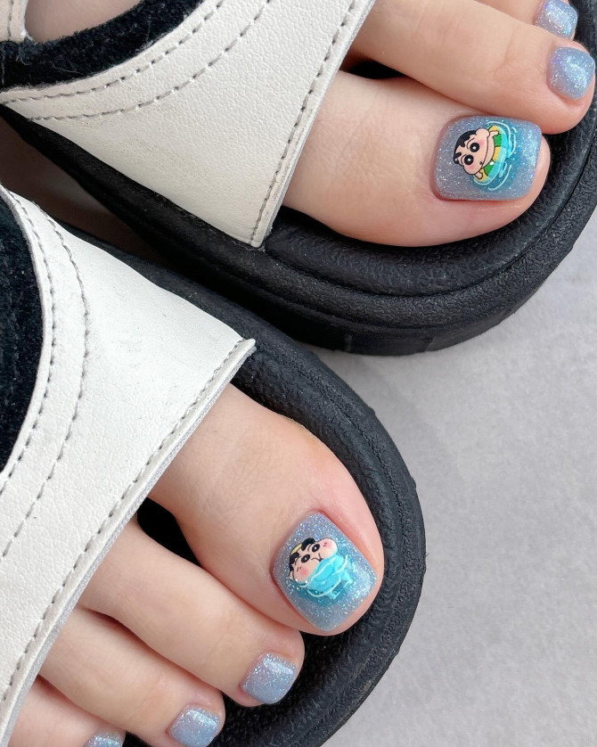 Toe nails with blue glitter polish and cartoon Shin-chan character art on big toes in wave-like design