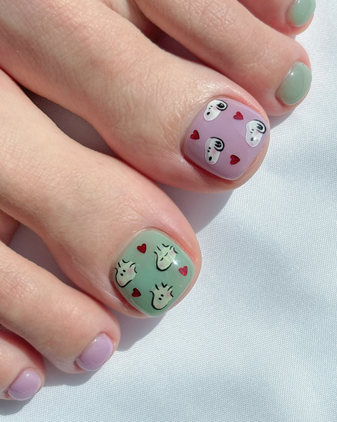 Toe nails in pastel green and lavender featuring Snoopy faces and small red hearts on short square nail shapes