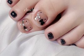 Toe nails with nude base, black bows, silver glitter accents and surrounding toes in sparkly black polish