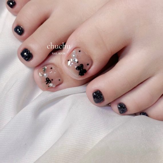 Toe nails with nude base, black bows, silver glitter accents and surrounding toes in sparkly black polish