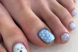 Toe nails with hand-painted white puppy, blue star background, and silver-blue glitter polish on short square nails